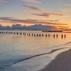 Zachód słońca nad spokojnym morzem, z rzędem drewnianych słupków na plaży Ulinia.