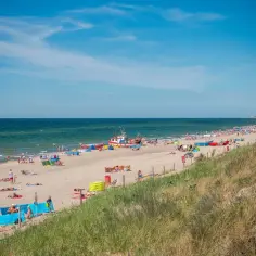 Słoneczna plaża w Dąbkach pełna wypoczywających ludzi i kolorowych parawanów. Warto tu przyjechać na wakacje!