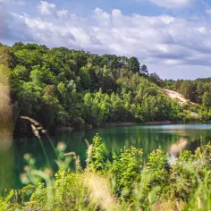 Turkusowe jezioro w wapnicy otoczone bujną zielenią. W oddali piaszczyste zbocze.