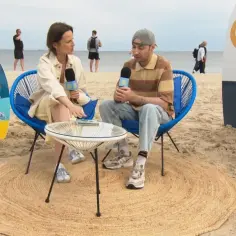 Wywiad na plaży w Świnoujściu. Dziennikarka z mikrofonem rozmawia z mężczyzną siedzącym na krześle. W tle widać morze i spacerujących ludzi.