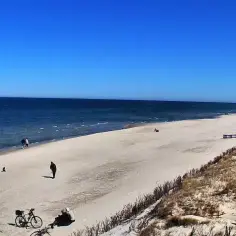 Plaża z widokiem na morze, kilka osób spaceruje, stoją rowery.