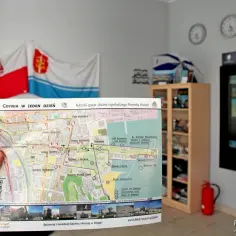 Mapa Gdynia w jeden dzień, pokazująca trasę spaceru po najmłodszym Pomniku Historii. W tle flagi i półka z pamiątkami.