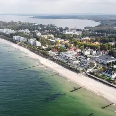 Widok z lotu ptaka na plażę w Mielnie, z zielonym morzem, piaszczystym brzegiem i zabudowaniami kurortu.