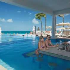 Para na wakacjach w hotelu nad morzem z basenem all inclusive, relaksuje się przy barze w wodzie.