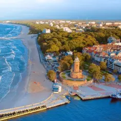 Widok z lotu ptaka na plażę, morze, molo, latarnię morską i nadmorskie miasteczko.