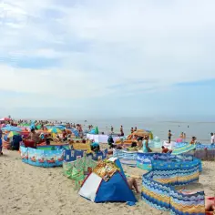 Słoneczna pogoda na sierpień nad morzem. Tłumy plażowiczów, kolorowe parawany i namioty chronią przed wiatrem.