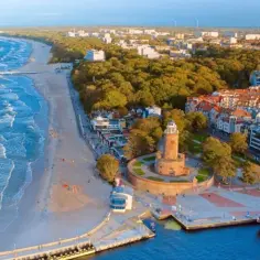 Widok z lotu ptaka na polski kurort nad Bałtykiem z latarnią morską, plażą i zabudowaniami.