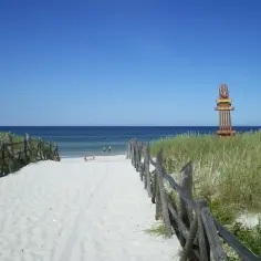 Piękna lubiatowo plaża z drewnianym płotkiem prowadzącym do morza. Na horyzoncie widać błękitne niebo i spokojną wodę.