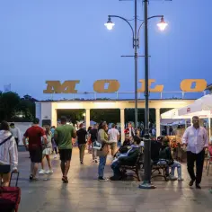 Ludzie spacerują pod napisem "MOLO", czuć atmosferę letnich **Sopot imprezy**. W tle widać kawiarnie i restauracje.