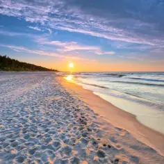 Zachód słońca nad morzem, piaszczysta plaża z śladami stóp, las w tle. Idealne, fajne miejsce nad morzem dla dwojga na romantyczny spacer.