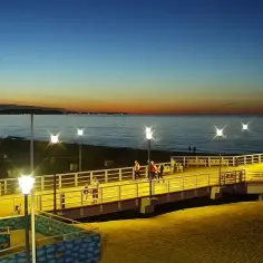 Wieczorny spacer po molo na jelitkowo plaży. Zachodzące słońce maluje niebo, a latarnie oświetlają ścieżkę.
