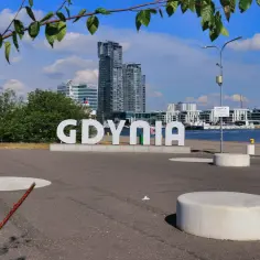 Witaj w centrum Gdyni! Widok na nowoczesne budynki, port i wielki napis "GDYNIA" na tle błękitnego nieba.