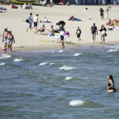 Ludzie cieszą się plażą, a jedna kobieta kąpie się w Bałtyku. Idealna temperatura wody w Bałtyku latem zachęca do relaksu.