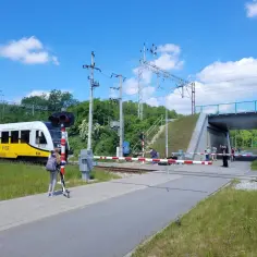 Dziewczynka na hulajnodze czeka przy przejeździe kolejowym PKP, gdy nadjeżdża pociąg.