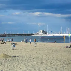 Ludzie odpoczywają na piaszczystej plaży w Sopocie, w tle widać molo i żaglówki.