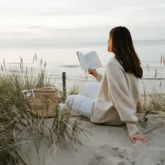 Kobieta czyta książkę na plaży, ciesząc się spokojem i świeżym powietrzem. To idealny moment, by poczuć, kiedy jest najwięcej jodu nad morzem.