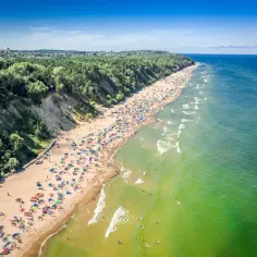 Tłum ludzi odpoczywa na piaszczystej plaży, wcinającej się w zielony las. Woda w morzu ma piękny, turkusowy odcień. To z pewnością najładniejsza plaża w Gdańsku.