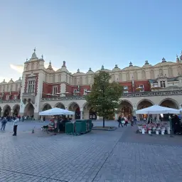Sukiennice, główna atrakcja w Krakowie, tętnią życiem. Ludzie spacerują po Rynku Głównym, podziwiając architekturę i kupując pamiątki.