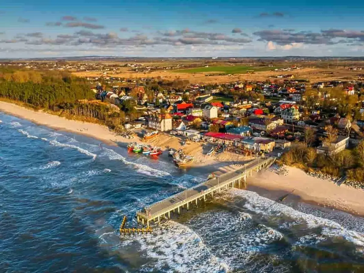 Widok na plażę z molo i kolorowymi łodziami. Idealne miejsce, gdzie nad morze z dziećmi tanio można wybrać się na wakacje.