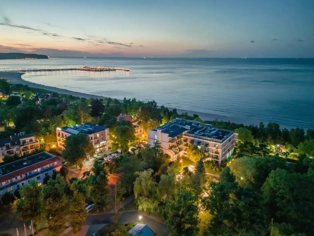 Idealny weekend majowy nad morzem. Widok na oświetlone apartamenty, plażę i molo o zmierzchu.