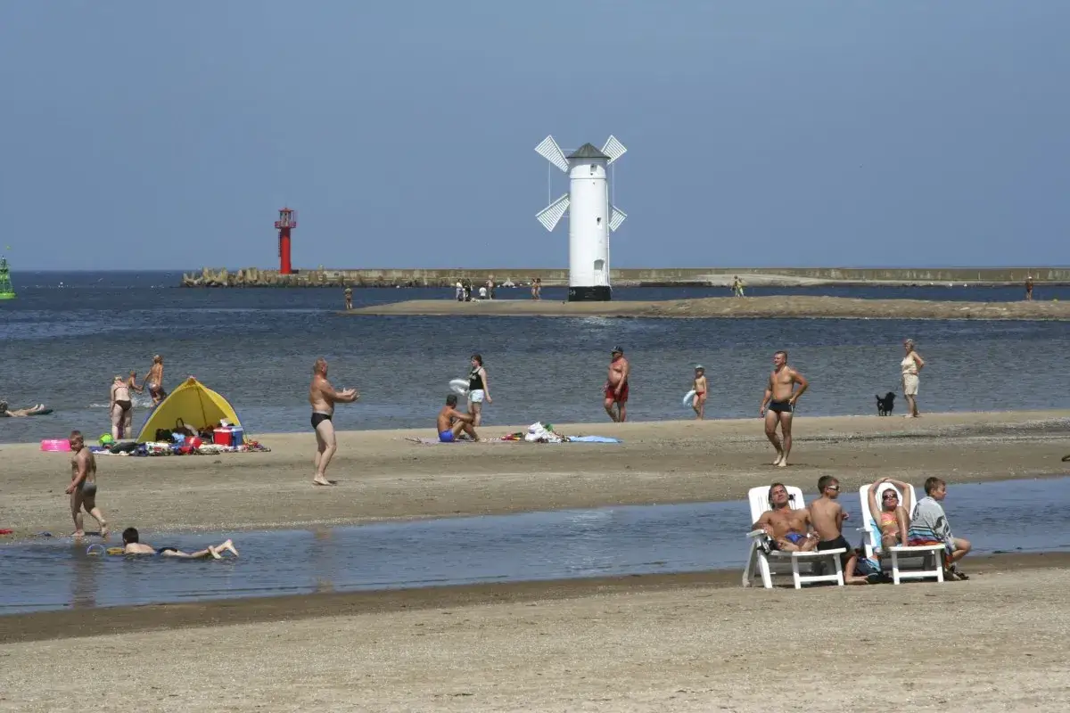 Promenada Świnoujście atrakcje: ludzie odpoczywają na plaży, w tle biały wiatrak i czerwona latarnia morska.
