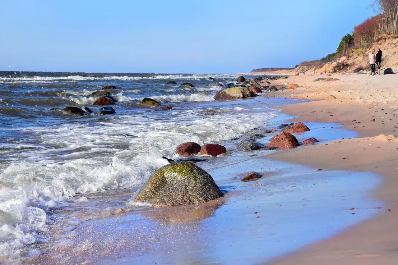 Kamienista plaża nad Bałtykiem, fale rozbijające się o brzeg. Dębina atrakcje to spacer po tej dzikiej plaży i podziwianie natury.